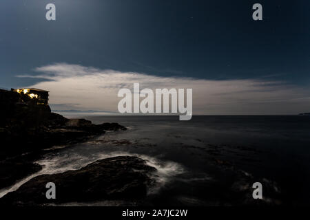 Night time view of a cliffside ocean view with a starry night sky and cirrus cloud and a cruise ship in the distance. Stock Photo