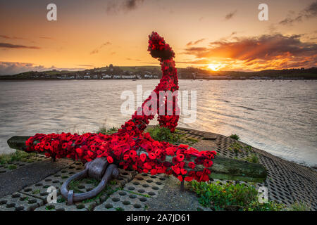 Appledore, North Devon, UK. Sunday 3rd November 2019. UK Weather. After a week of strong winds and heavy downpours in North Devon, overnight the weatherfront clears away. At dawn on the River Torridge estuary the sun starts to light up the Appledore Anchor, covered by the local community with knitted poppies in preparation for the forthcoming Remembrance Sunday. Credit: Terry Mathews/Alamy Live News Stock Photo