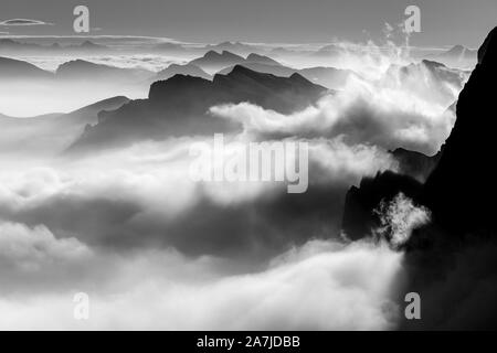 Moving clouds above the valley at sunrise. Evocative tide of clouds. Black and white mountain landscape. The Dolomites. Italian Alps. Europe. Stock Photo