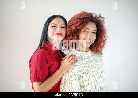 Curly red-haired woman standing near her Asian excited friend Stock Photo
