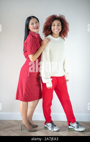 Friends wearing stylish bright clothing standing near wall Stock Photo