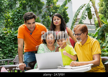 Happy Multi-Generation Family in-courtyard together doing video chat on laptop In-garden home Stock Photo