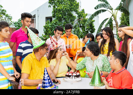 Group-Of Happy Big Families Celebrating birthday mother Feeding her Daughter Cake at-courtyard of-their home Stock Photo