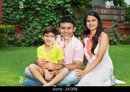 Happy Family Father And Mother With Little son Sitting on the grass and Relaxing At park Stock Photo