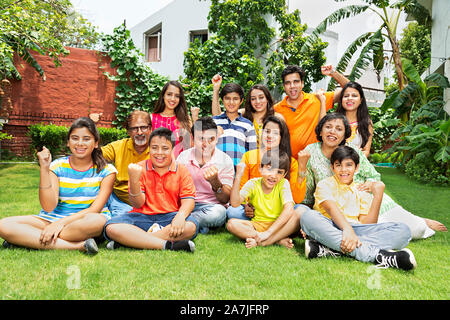 Group Of Big Families Members Sitting-on-grass Together and Fists-Hand Winning Success Celebration in-Courtyard Of-their House Stock Photo