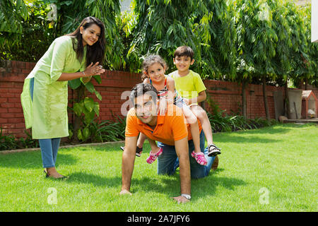 Happy Young Family Two Kids Riding on Dad back With Mom In-Outdoor Park Stock Photo