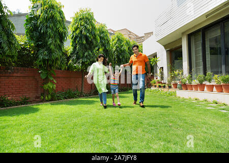 Happy Young Family Parents Lifting-up Kid daughter And Running in-Courtyard of-their House Stock Photo