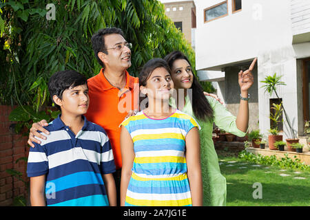Happy Family Parents And Two Children Standing Together And Pointing to Somewhere in-courtyard Near their home Stock Photo