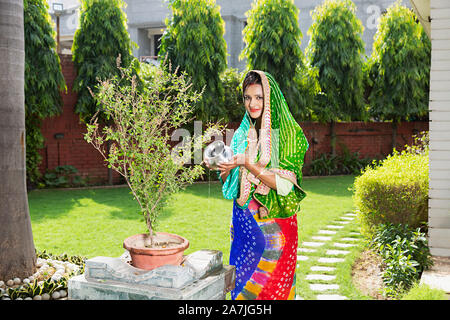 Indian Hindu Traditional Woman in Traditional Wear Pouring Water Ocimum Tulsi Plant in-Courtyard Of-Their House Stock Photo