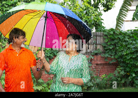 Happy Loving Senior Couple with umbrella in the rain Having Fun Enjoying in the garden Stock Photo