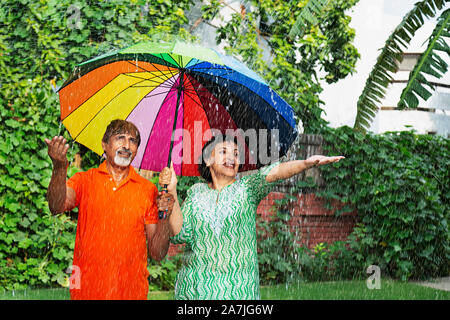 Happy Loving Elderly Couple under umbrella Enjoying the rain At-park Stock Photo