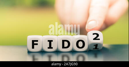 Hand turns a dice and changes the expression "FIDO1" to "FIDO2". Stock Photo
