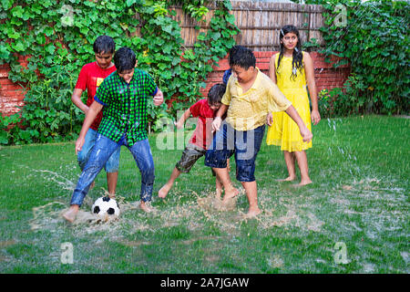 happy indian Children Friends Playing Soccer ball game In-The Rain In-garden on Rainy weather