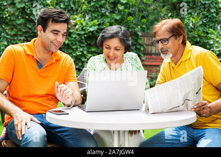 Happy Family Sitting-in garden home Senior Father And Mother With Adult Son Using Laptop With Newspaper in-morning Stock Photo