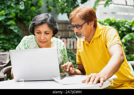 Elderly Couple Looking-at Laptop Screen in-garden home on Summer Morning Stock Photo