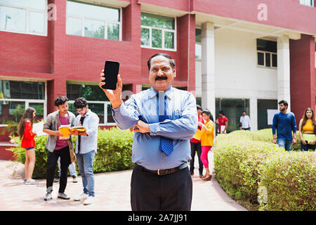 Senior man College Teacher Showing Mobile-Phone With Students-In-The-Background In-Outside Campus Building Stock Photo