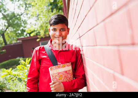 Young Teenage Boy College Student Holding Book Standing Leaning against wall College Campus Building Stock Photo