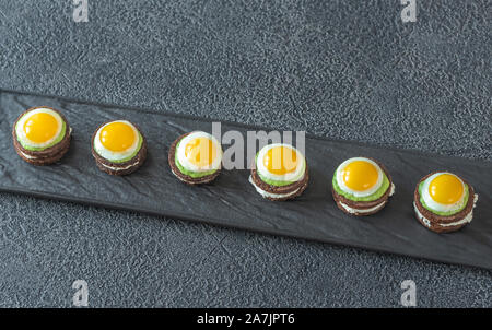 Canape with cream cheese, guacamole and fried quail eggs on the plate Stock Photo