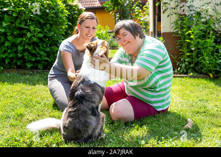 mentally disabled woman with a second woman and a companion dog, concept learning by animal assisted living Stock Photo