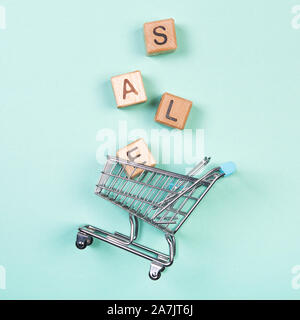 A miniature shopping cart and wooden blocks with the wordings SALE, isolated against mint background. Stock Photo