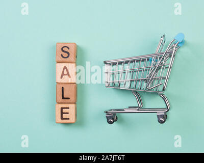 A miniature shopping cart and wooden blocks with the wordings SALE, isolated against mint background. Stock Photo