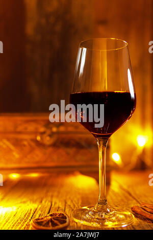 Hot mulled wine (red wine) in a shiny red wine glass on wooden table, decorated with Christmas season spices cinnamon sticks and slice of orange Stock Photo