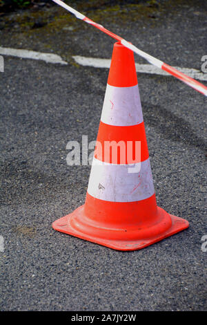 close-up on an orange white traffic cone with red-white caution tape at a street construction site, traffic cone on street for people safety Stock Photo