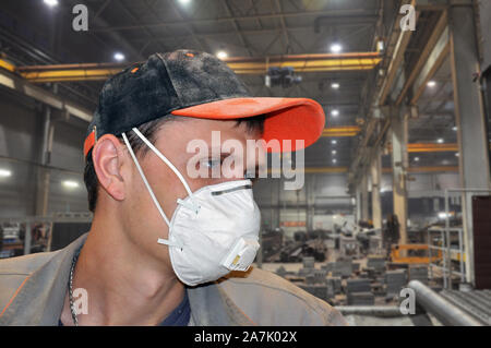 Young man in a dust mask and dusty cap at work. Personal protective equipment Stock Photo