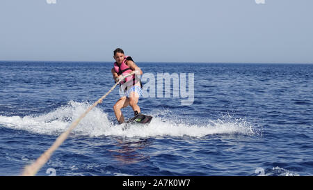 A man wakeboarder clings to a cable and moves behind a boat on the sea Stock Photo