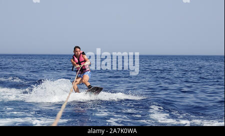 A man wakeboarder clings to a cable and moves behind a boat on the sea Stock Photo