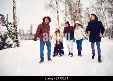 Group of friends enjoying pulling a sled in the snow in winter Stock Photo