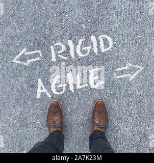 A man in leather shoes stands in front of the words "Rigid" and "Agile" with arrows pointing left and right Stock Photo