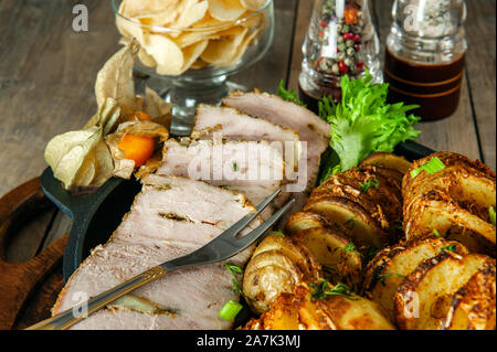 A piece of baked stuffed meat with potatoes and vegetables in a frying pan and a wooden Board. Stock Photo