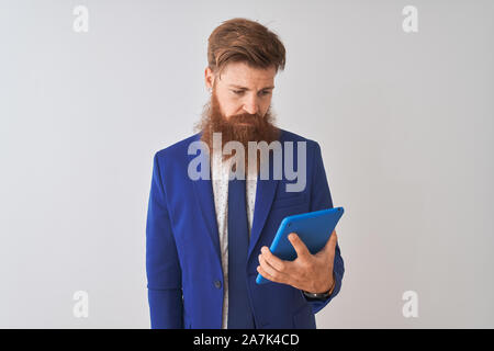 Young redhead irish businessman using tablet over isolated white background with a confident expression on smart face thinking serious Stock Photo