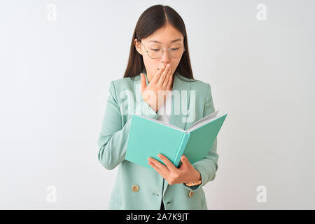 Young chinese student woman wearing glasses reading book over isolated white background cover mouth with hand shocked with shame for mistake, expressi Stock Photo