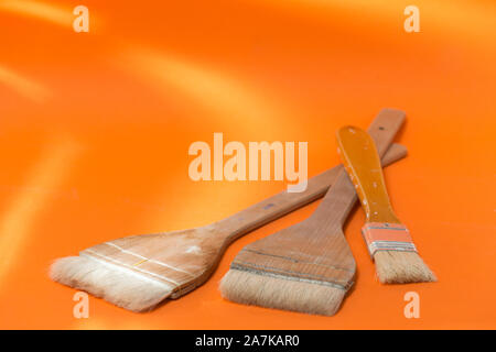 three painter brushes of different size, placed on an orange surface Stock Photo