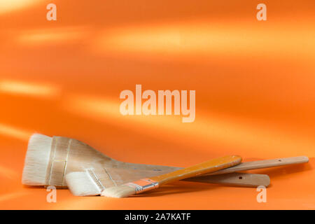 three painter brushes of different size, placed on an orange surface Stock Photo