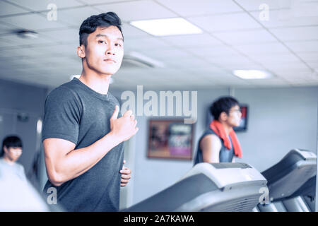 Handsome young atheletic man in sportswear running on treadmill at gym Stock Photo