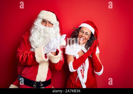 Middle age couple wearing Santa costume and glasses over isolated red background clapping and applauding happy and joyful, smiling proud hands togethe Stock Photo