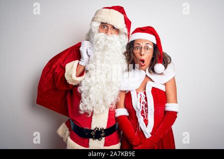 Senior couple wearing Santa Claus costume holding sack over isolated white background scared in shock with a surprise face, afraid and excited with fe Stock Photo