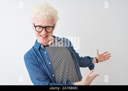 Young albino blond man wearing denim shirt and glasses over isolated white background Inviting to enter smiling natural with open hand Stock Photo