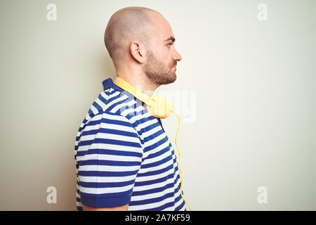 Young man listening to music wearing yellow headphones over isolated background looking to side, relax profile pose with natural face with confident s Stock Photo
