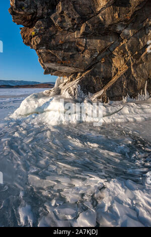 Many thin broken ice plates next to a large rock on Lake Baikal. A lot of cracked ice. Sunny. Clear blue sky. Vertical frame. Stock Photo