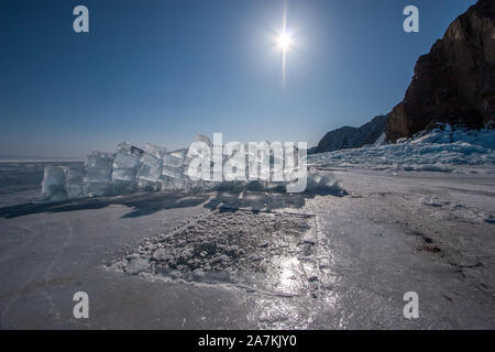 An ice hole and ice cubes from it piled into the wall on a sunny day. Clear blue sky with the sun. Big rock nearby. Stock Photo