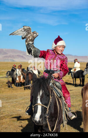 Young Mongolian boy in traditional Mongolian dress holding his falcon on horseback. Young children start training with falcons prior to working with g Stock Photo