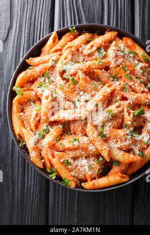 Italian penne pasta alla vodka topped with parmesan and parsley close-up in a plate on the table. Vertical top view from above Stock Photo