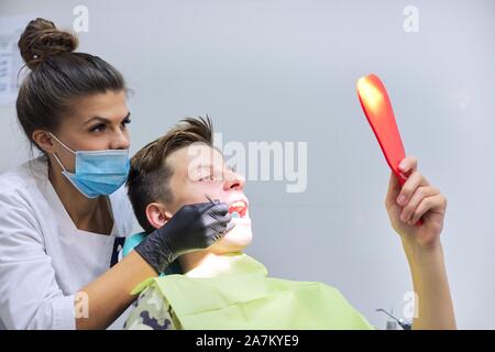 Teen boy on visit to the dentist sitting in chair, young woman doctor treating teeth Stock Photo