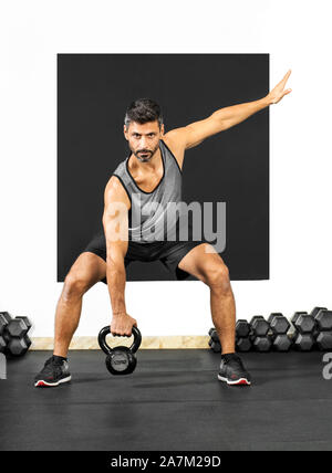 Man doing exercises with a kettlebell weight in a gym lifting it in the squat position to strengthen his gluteus muscles and legs in a health and fitn Stock Photo