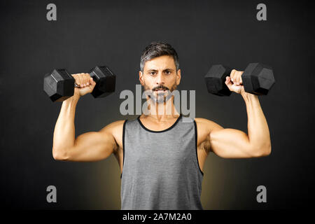 Fit muscular man weightlifting with dumbbells in a gym doing bodybuilding exercises to strengthen his muscles in a health and fitness concept Stock Photo