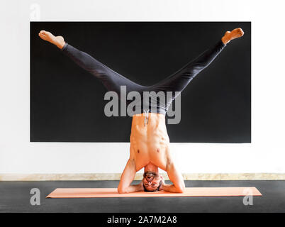 Athletic man doing a sirsasana heastand exercise while practising yoga in a gym in a health and fitness concept Stock Photo